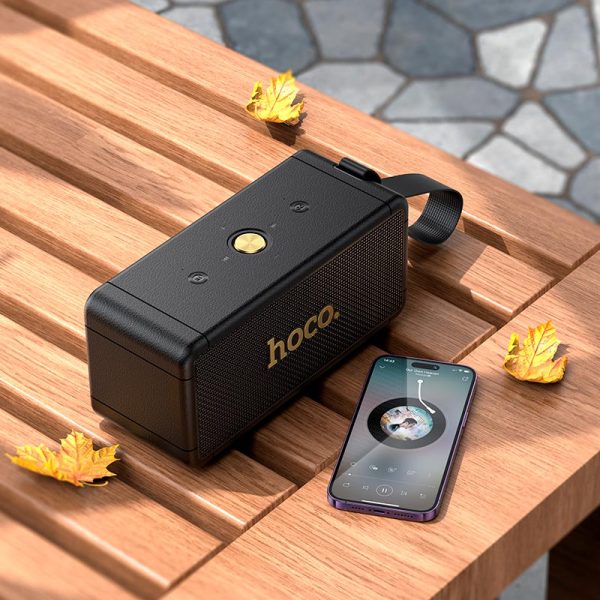 Parlante HOCO HT1 Max negro en una mesa de madera al aire libre con hojas de otoño
