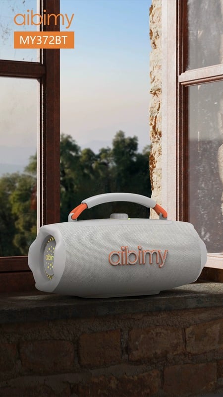 Parlante AIBIMY MY372BT gris y naranja apoyado en una ventana con vista al campo
